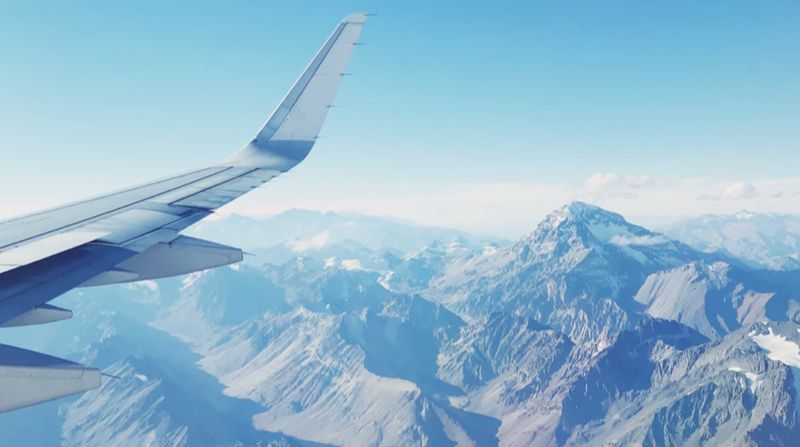A picture from a window on a plane looking down onto a mountainous range below. The airplane wing is also partly in view as well.